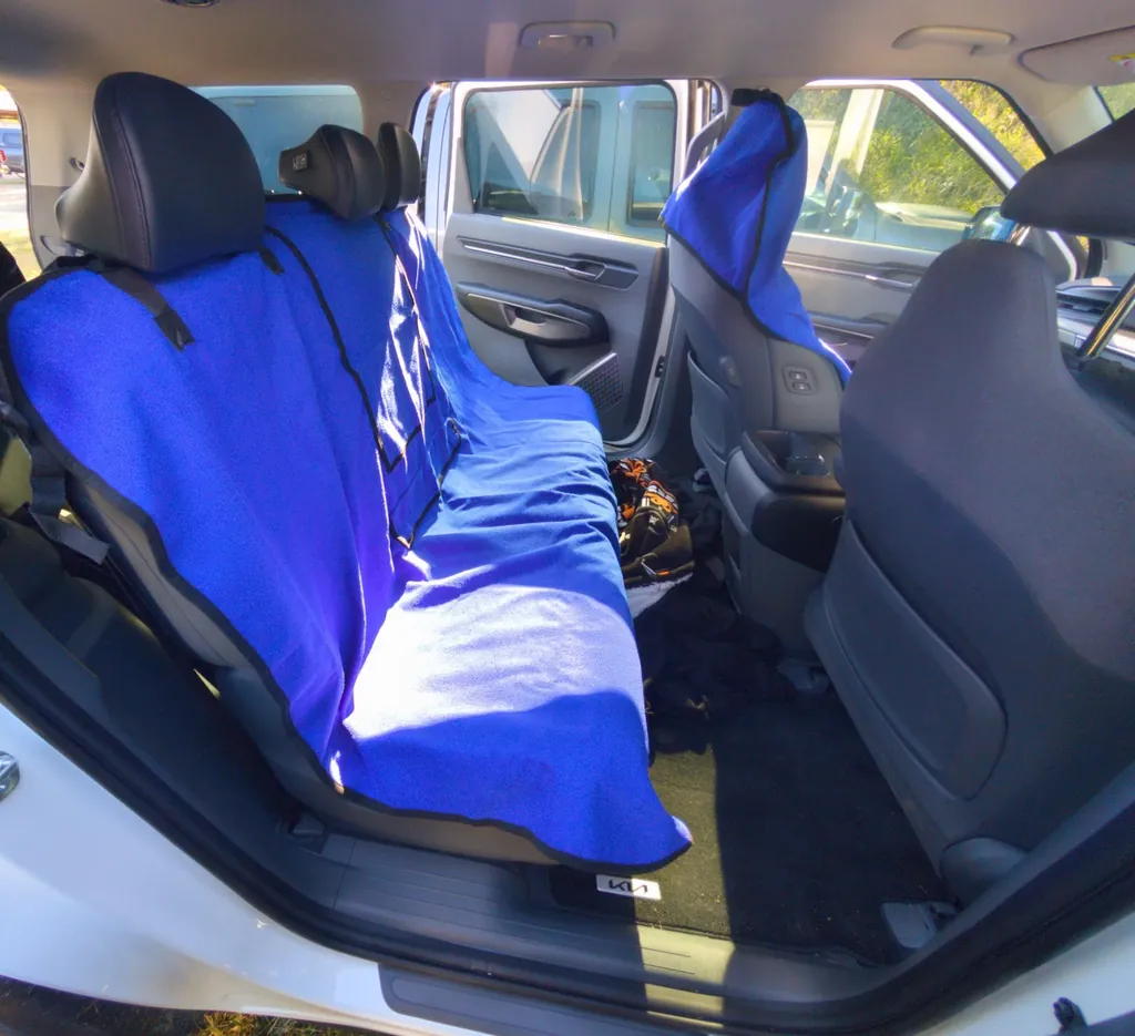 The EV9’s middle-row bench seen through the open rear door, covered with blue towel seat covers.